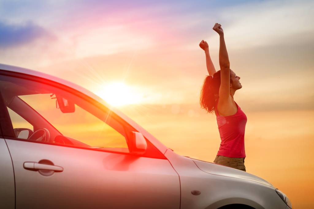 Woman proudly standing in front of car and sunset