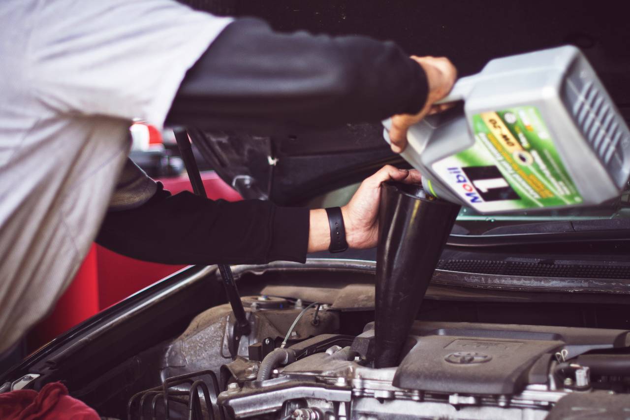 mechanic filling motor oil in car engine